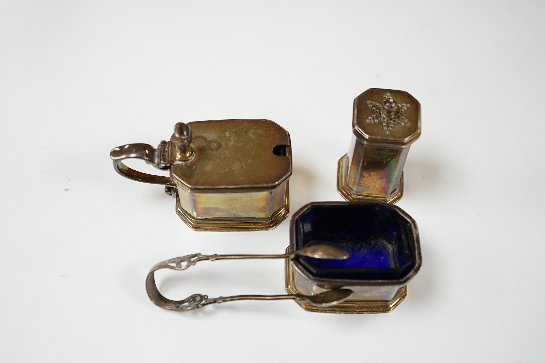 A George V silver three piece condiment set by S.W. Smith & Co, Birmingham, 1917/8/9 and a pair of silver tongs.
